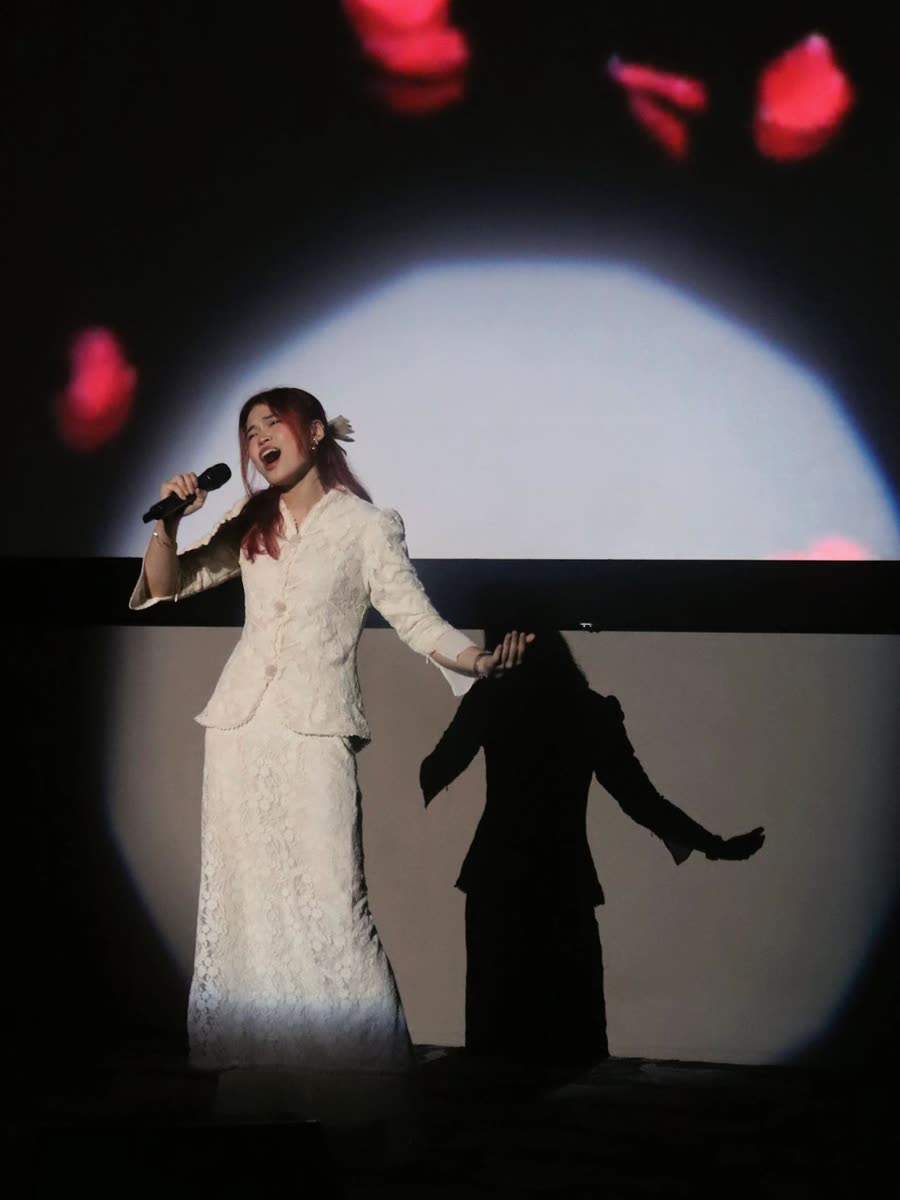 Trisha singing in a spotlight in a white kebaya
