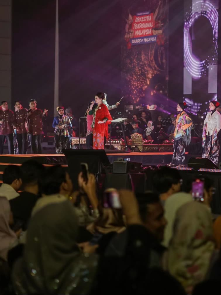 Trisha in a red kebaya singing with a traditional orchestra