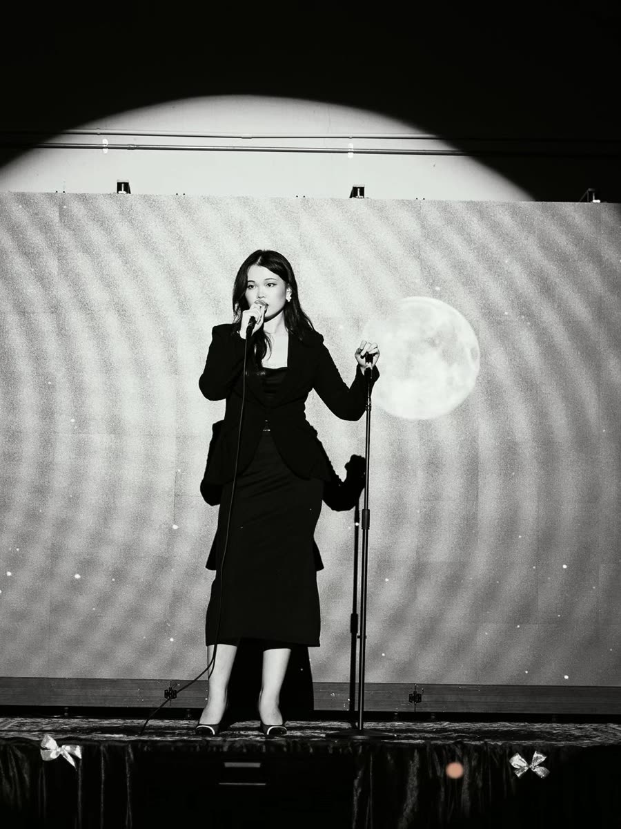 Trisha singing on a dark stage, in black and white